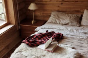 the bedroom in a well-maintained texas cabin with an open book and red plaid blanket on the bed