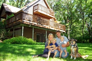 happy couple smiling with their kids and dog on the lawn outside of their custom-built cabin