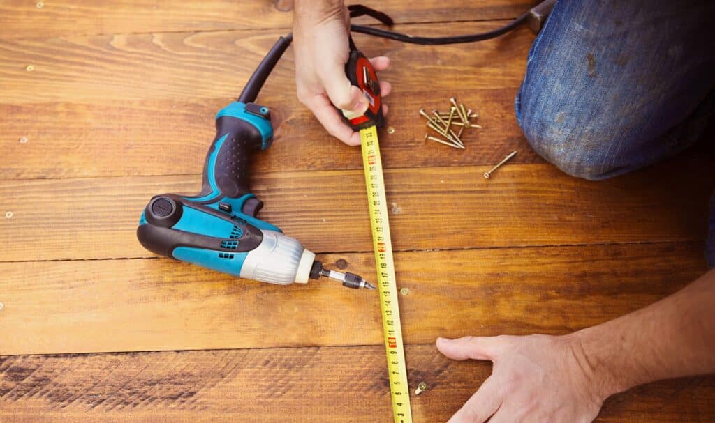 cabin owner's hands holding measuring tape next to electric drill on top of wooden slats