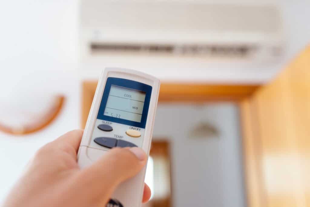 homeowner pointing a white remote control at their white ductless ac unti