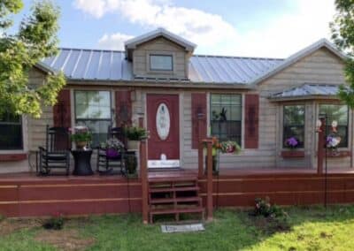 front exterior of a custom texas cabin built by ormeida with red front door, light grey siding and silver metal roof