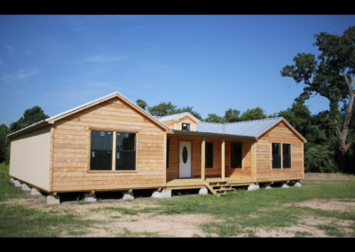 front exterior of a custom texas cabin built by ormeida with natural wood and silver metal roof