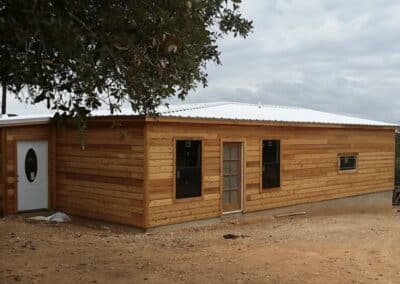 front exterior of a custom texas cabin built by ormeida with natural wood and silver metal roof