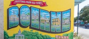 A colorful mural reading “Greetings from Old Town Boerne, Texas” painted on a yellow brick wall