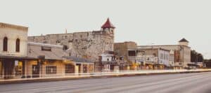 A historic Texas main street with stone buildings and storefronts, captured with light streaks from passing traffic